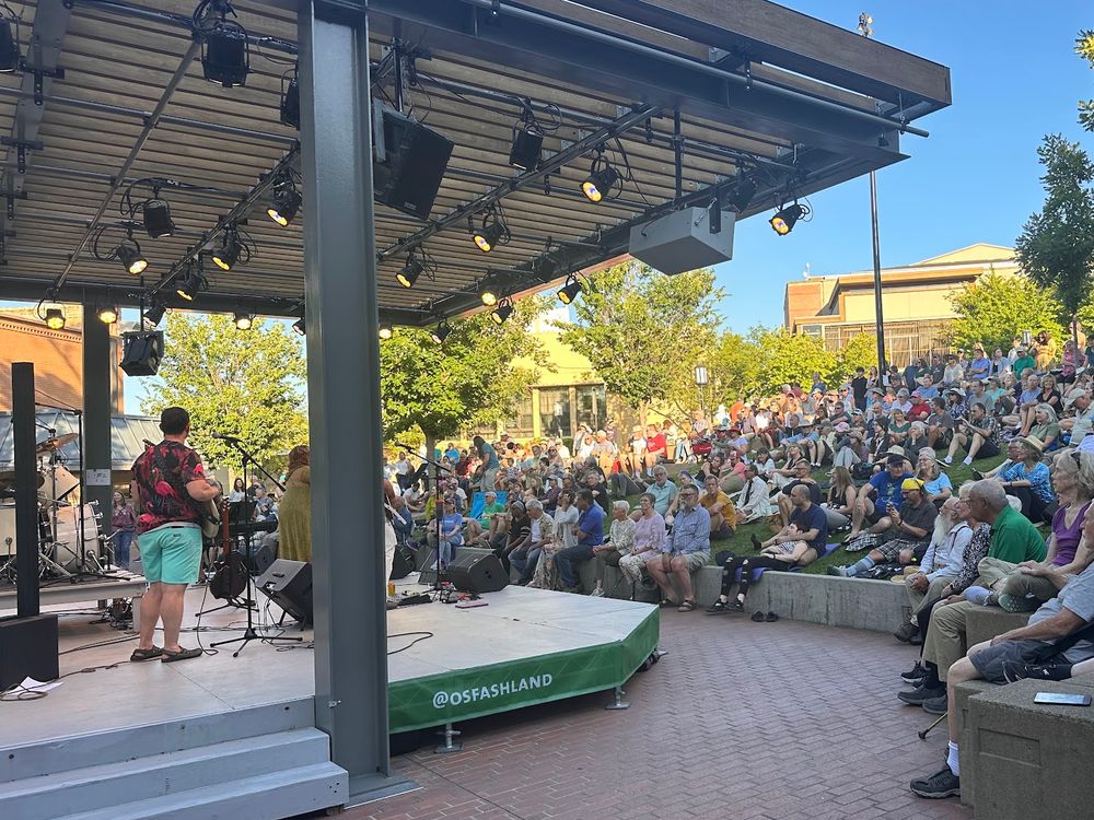 The Green Show at 7:11 PM, seen from beside the stage, people seated on the steps up the hill